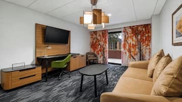 A modern living room with a flat-screen TV mounted on a wooden wall, a desk with a chair, a sofa, and a patterned carpet.