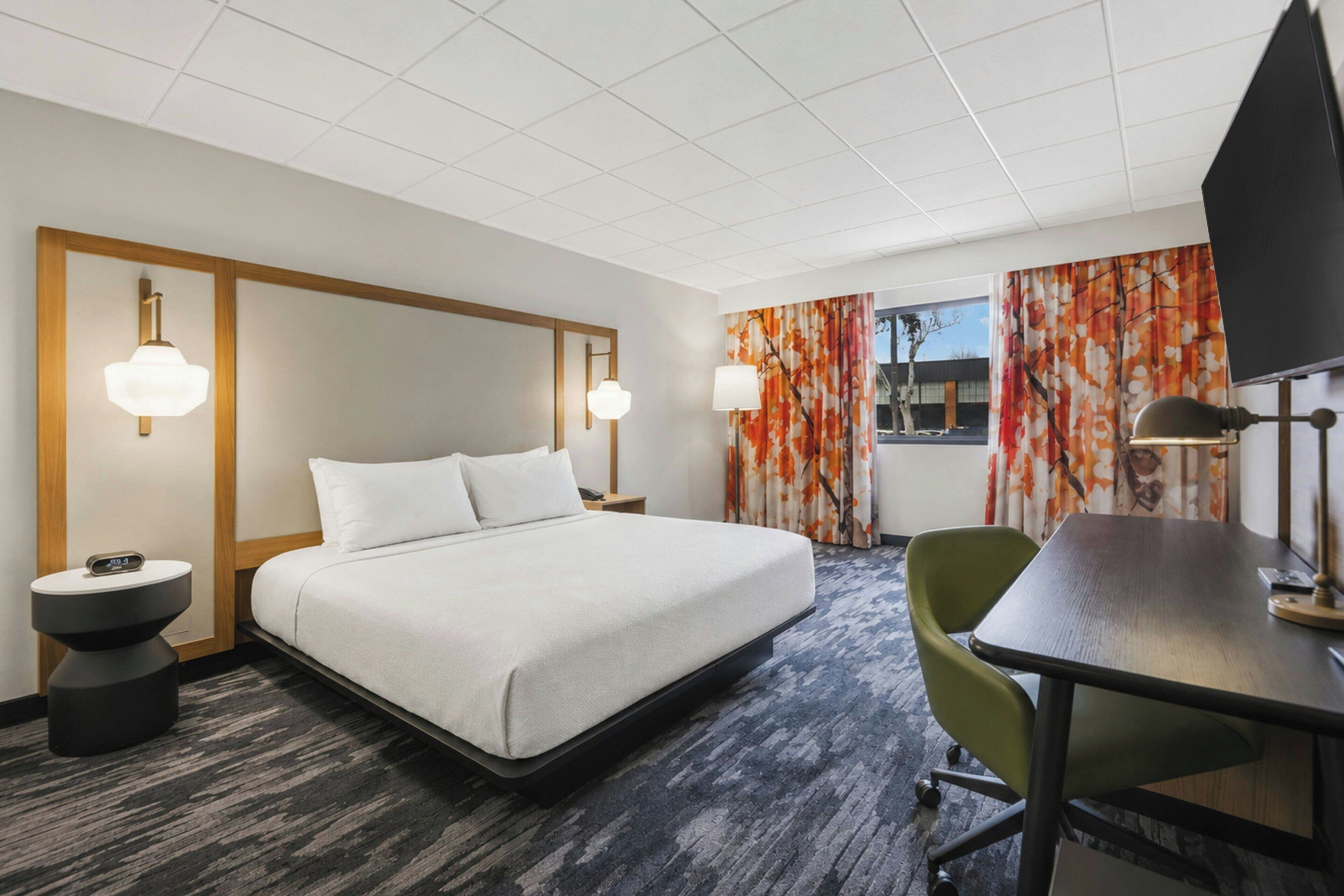 A hotel room with a bed, bedside tables, a desk, a chair, and a window with curtains.