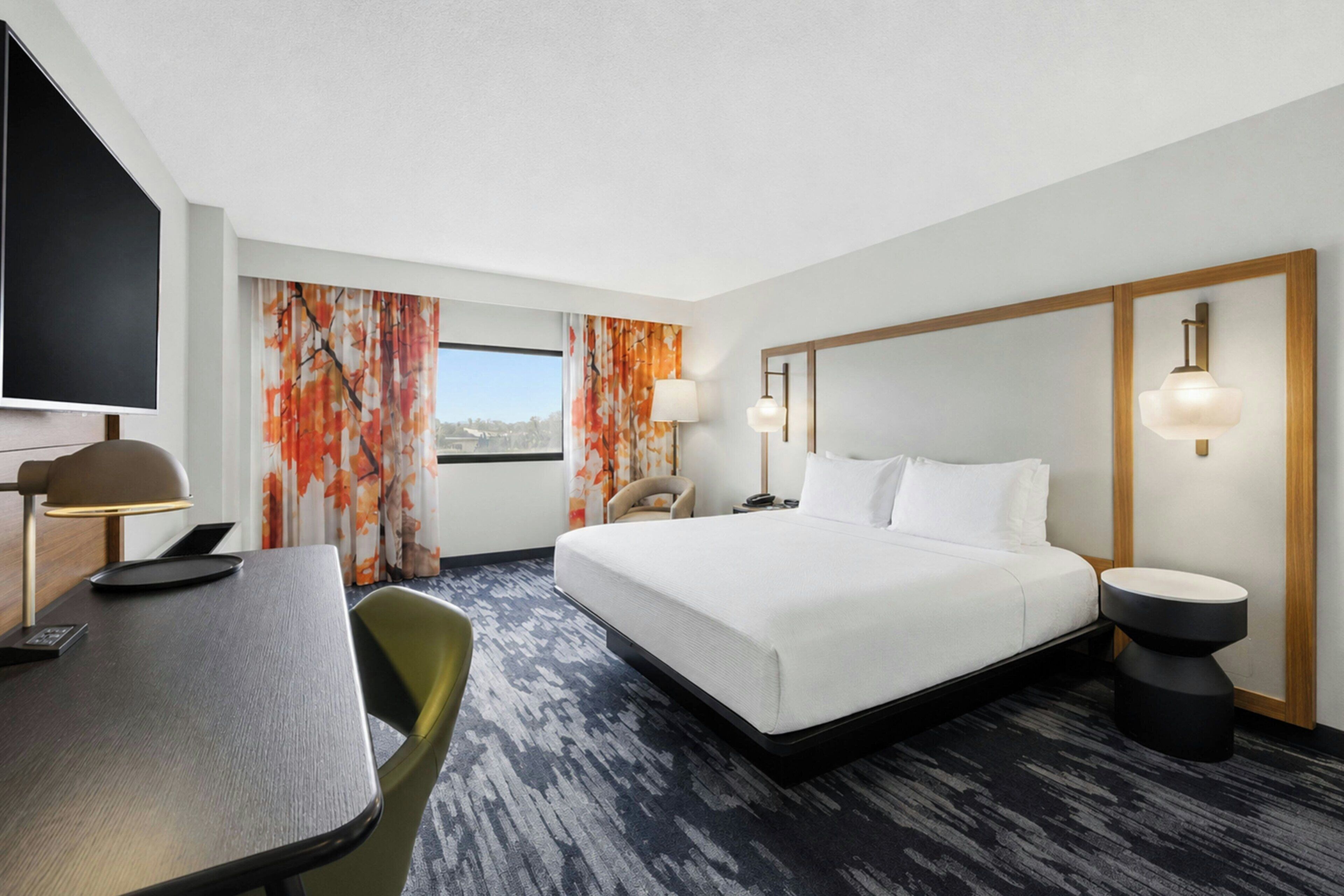 A hotel room with a bed, a desk, a chair, a TV, and a window with curtains.