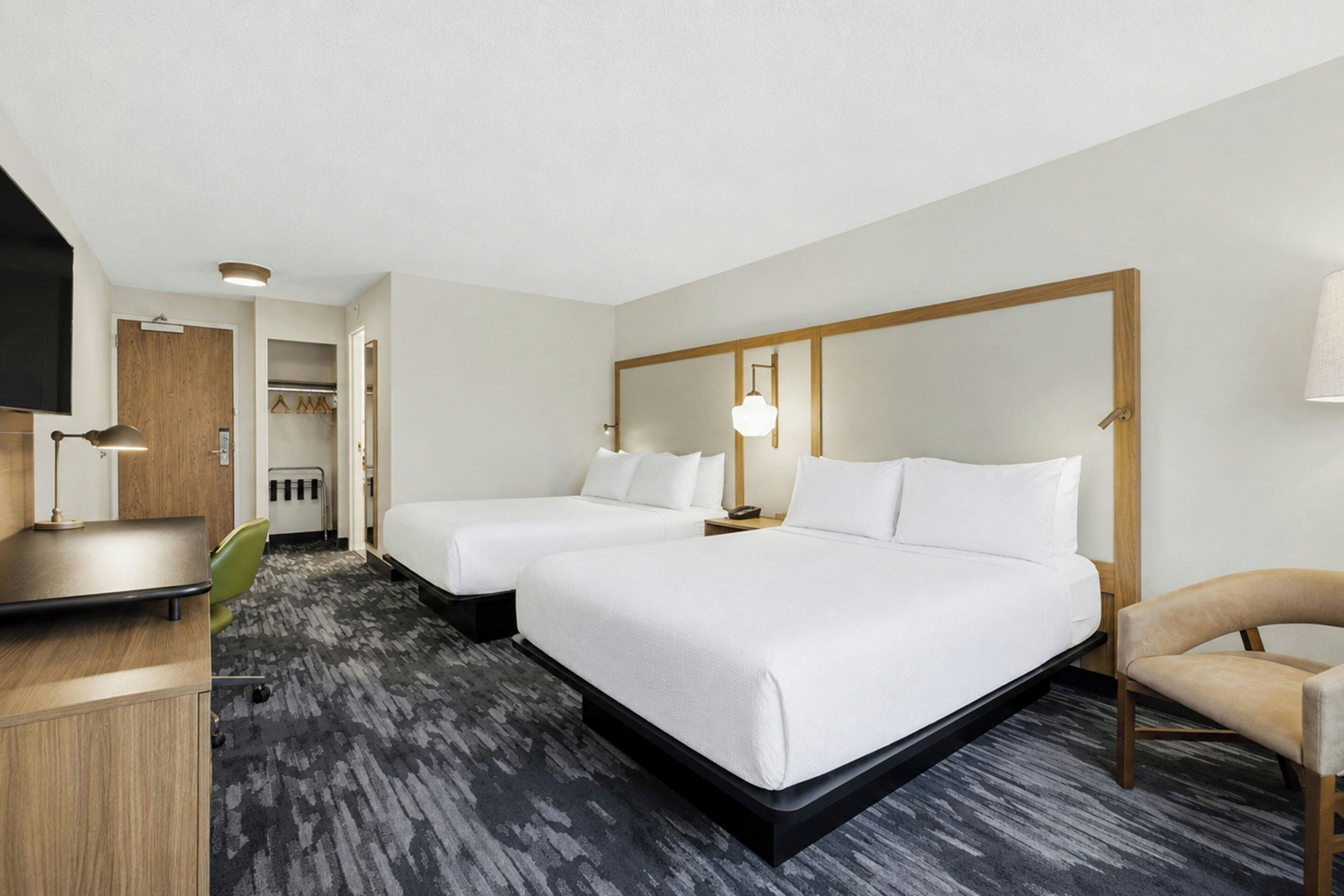 A hotel room with two beds, a desk, a chair, and a television.