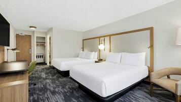 A hotel room with two beds, a desk, a chair, and a television.