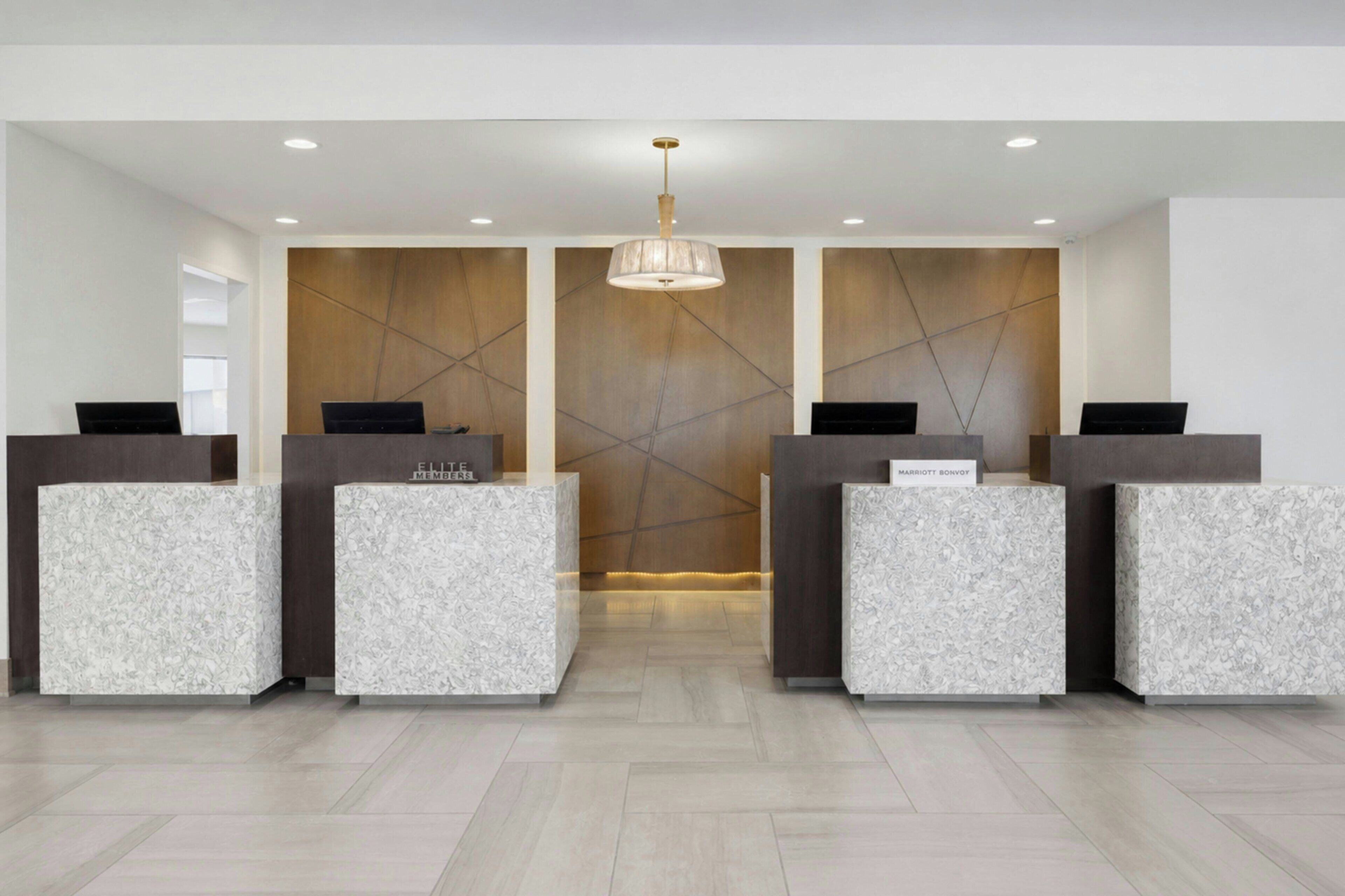 A reception area with three reception desks, each labeled with a hotel name, and a modern chandelier.
