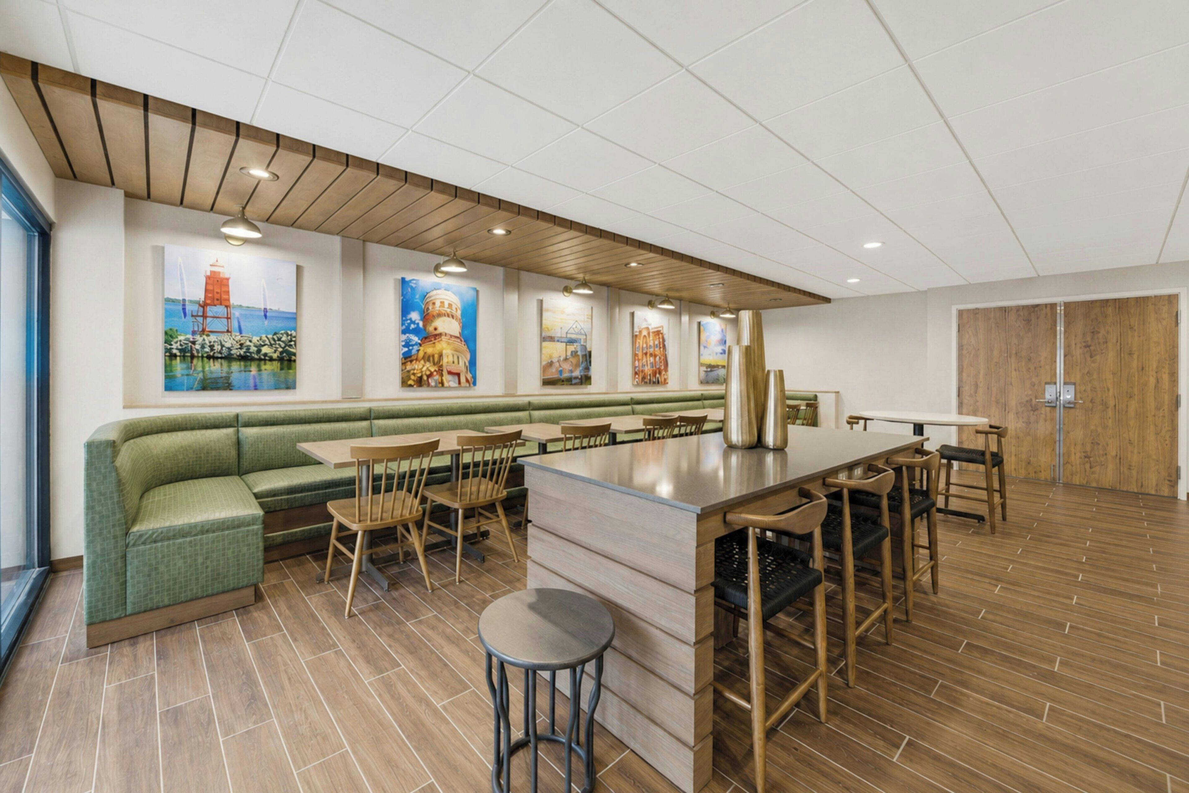 A modern restaurant with a green booth seating area, wooden tables, and a bar counter.