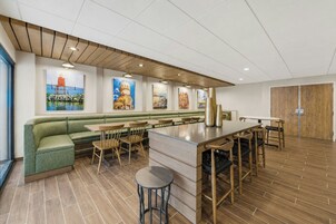 A modern restaurant with a green booth seating area, wooden tables, and a bar counter.