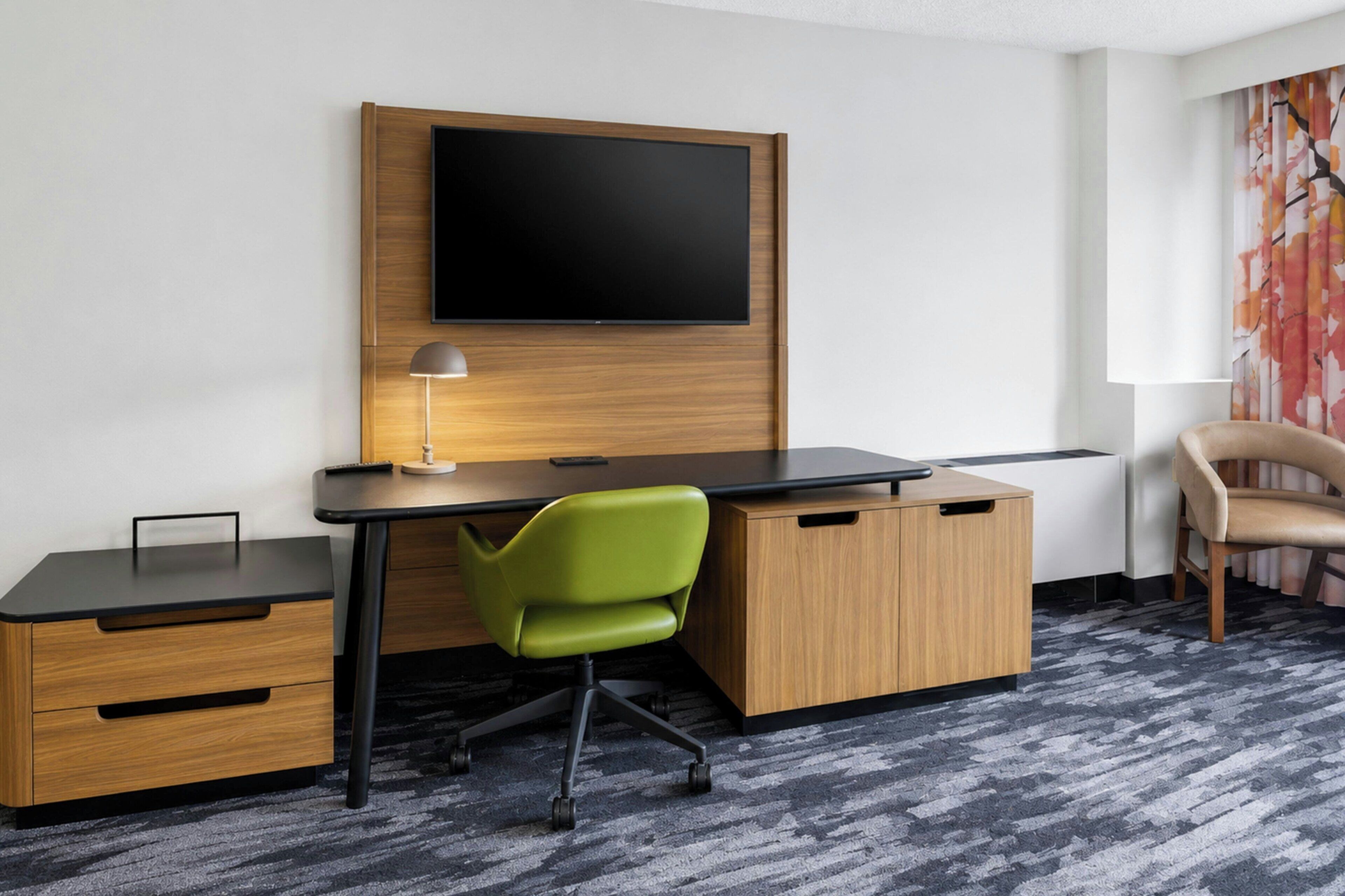 A hotel room with a desk, chair, TV, and a window with curtains.