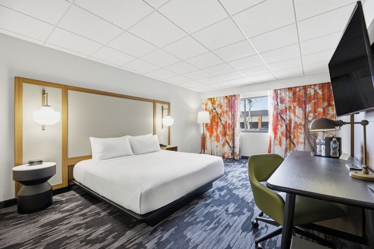 A hotel room with a bed, bedside tables, a desk, a chair, and a TV.
