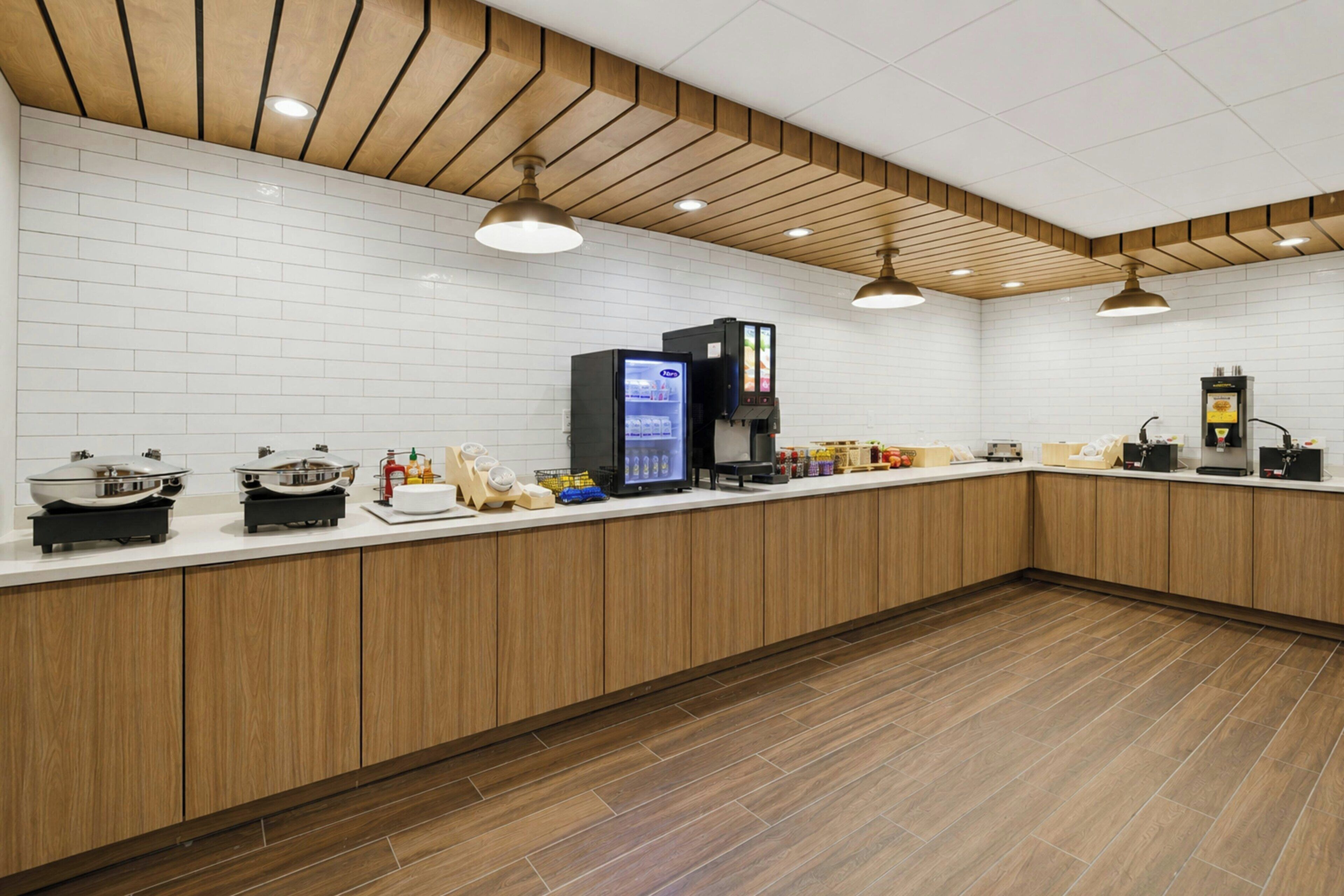 Un espace cuisine moderne avec un dosseret de carrelage blanc, des armoires en bois et un plan de travail agrémenté de divers appareils et condiments.
