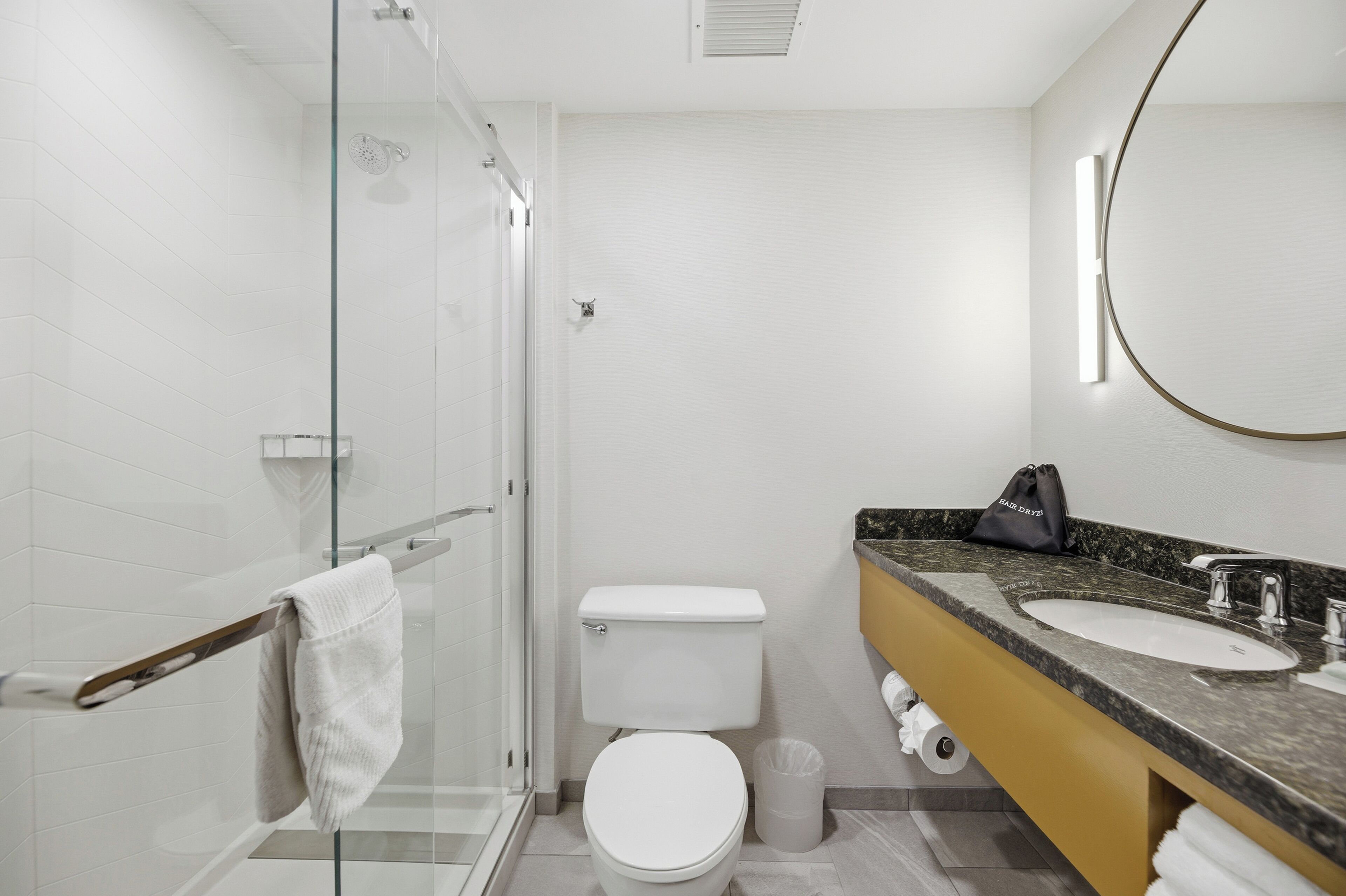 A modern bathroom with a glass shower enclosure, a white toilet, a sink with a marble countertop, and a towel rack.