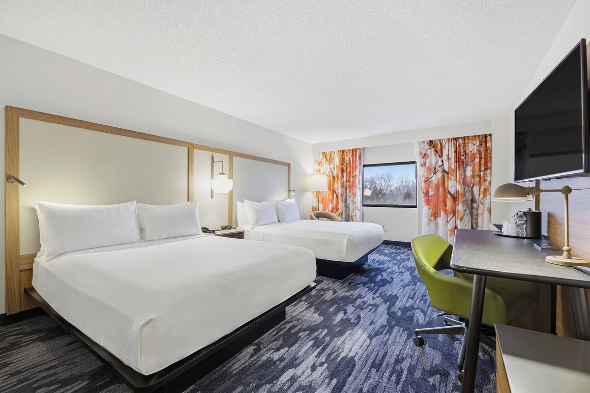 A hotel room with two beds, a desk, a chair, and a TV.