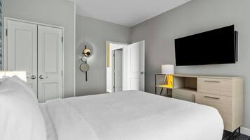 A hotel room with a bed, a desk with a chair, a flat-screen TV, and a door.
