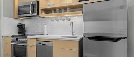 A modern kitchen with a built-in microwave, oven, and dishwasher, wooden cabinets, and a stainless steel refrigerator.