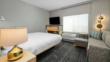 A hotel room with a bed, a desk, a television, a sofa, and a window.