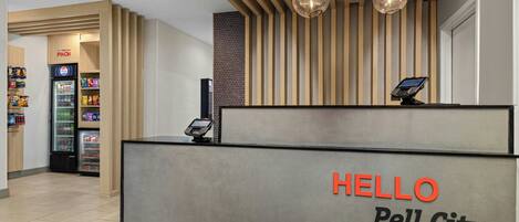 A reception desk with a 'HELLO Pell City' sign, a vending machine, and a counter with a payment terminal.