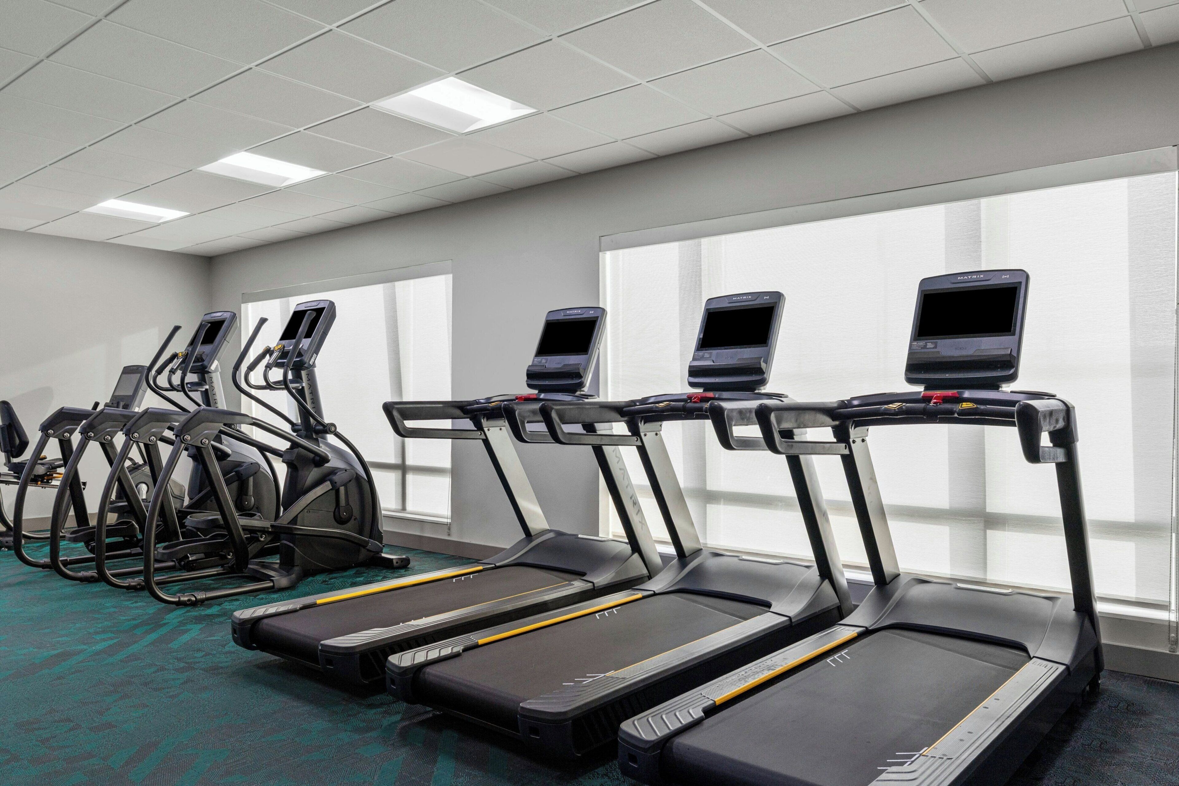 Un gimnasio con cintas de correr, elípticas y bicicletas estáticas, equipado con pantallas digitales.