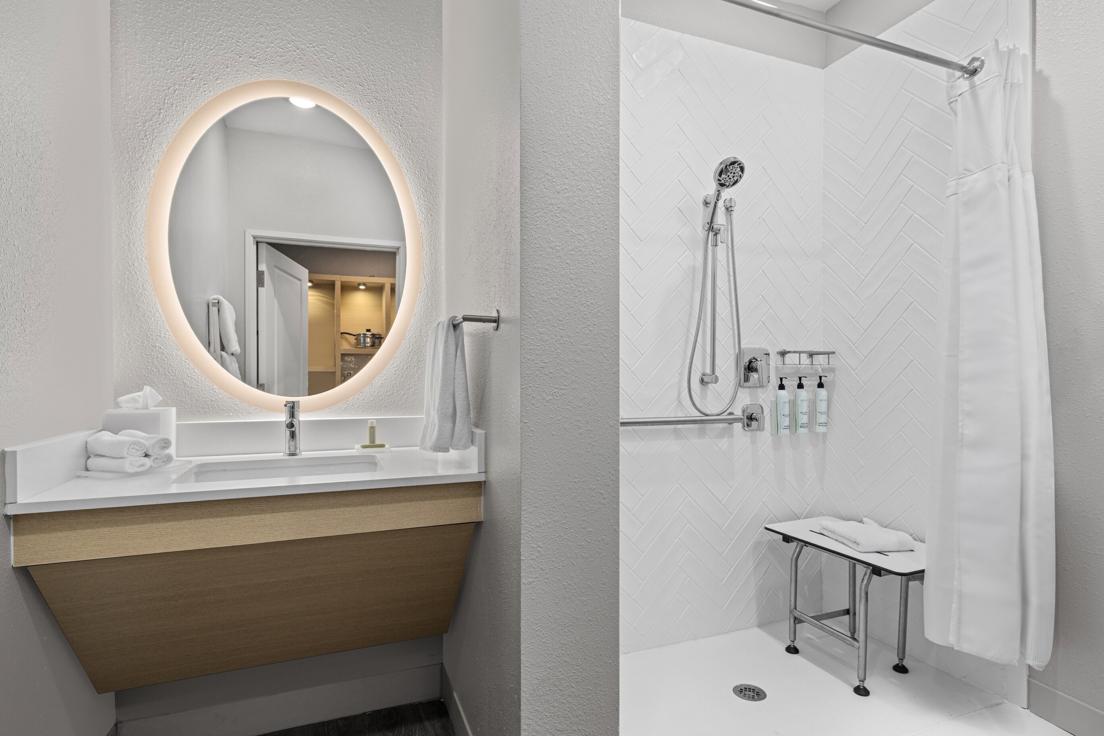 A bathroom with a mirror, sink, shower, and a towel rack.