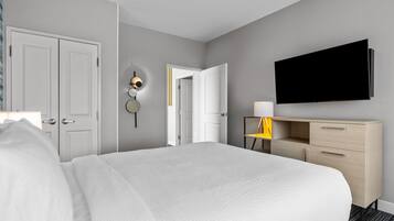 A hotel room with a bed, a desk with a lamp, a flat-screen TV, and a door leading to another room.
