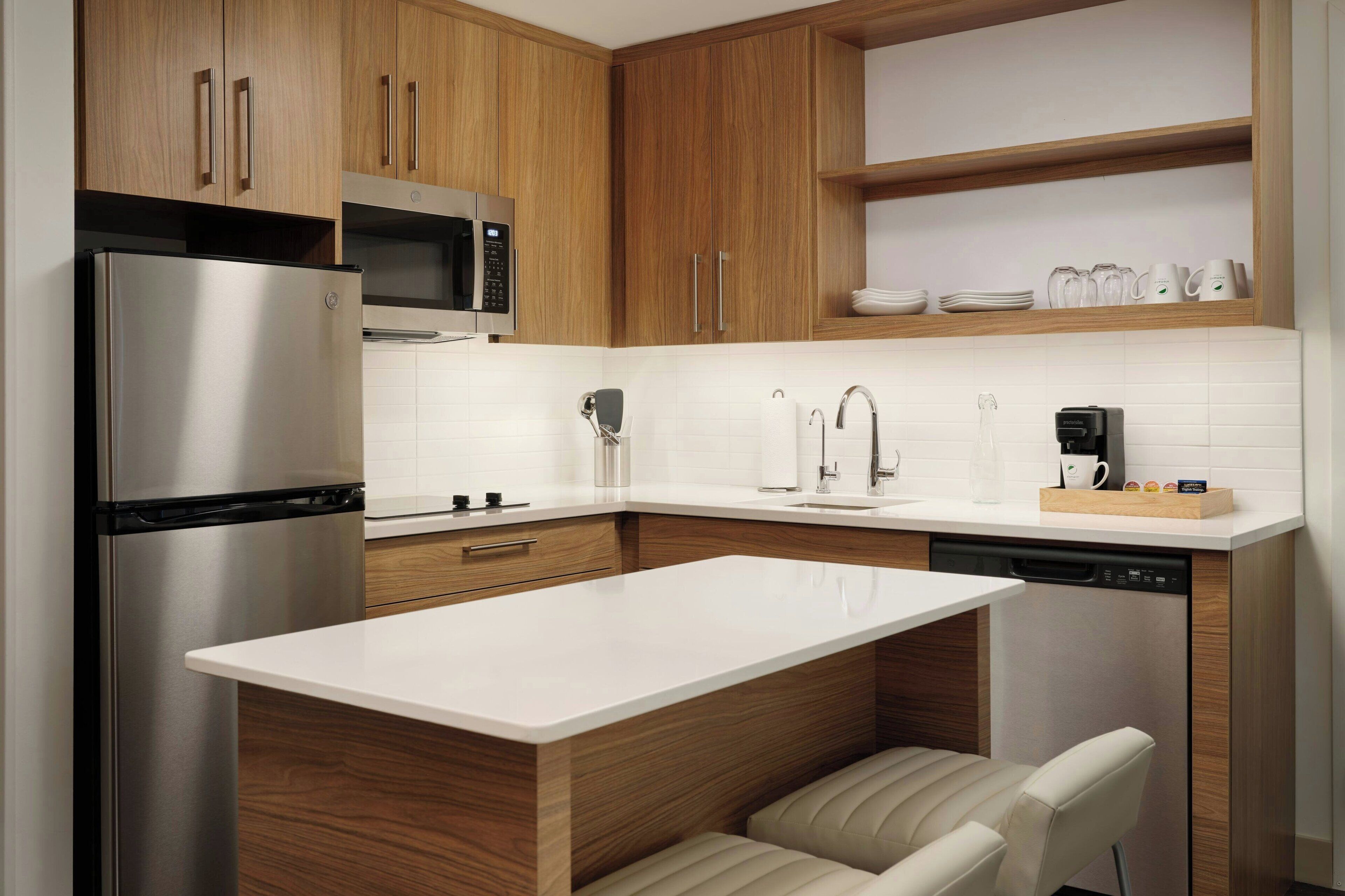 A modern kitchen with wooden cabinets, stainless steel appliances, a white countertop, and a built-in dishwasher.