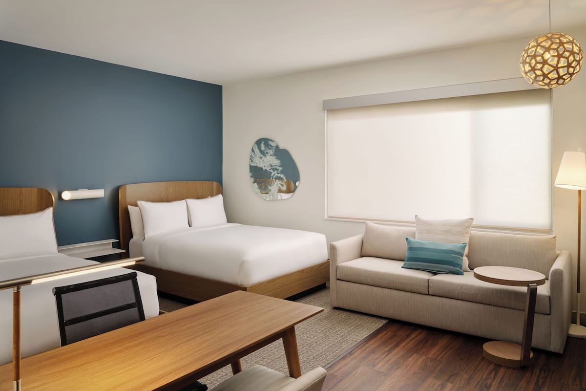 A hotel room with a bed, a sofa, a desk, and a lamp.
