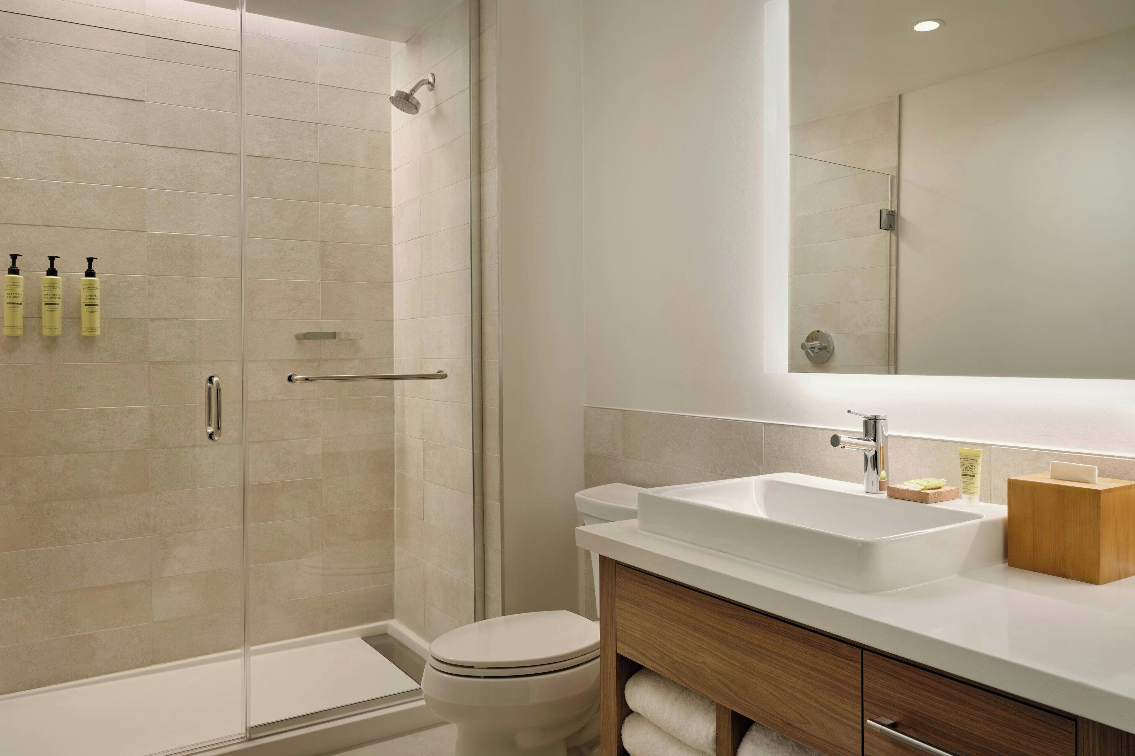 A modern bathroom with a glass shower enclosure, a white sink, and a wooden vanity.