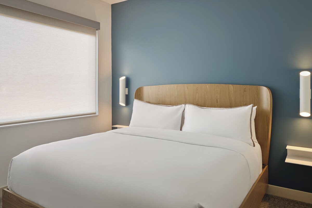 A neatly made bed with white linens in a room with a blue accent wall and a wooden headboard.