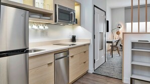 A modern kitchen with a stainless steel refrigerator, microwave, and dishwasher. There is a coffee maker on the counter, and a dining area is visible in the background.