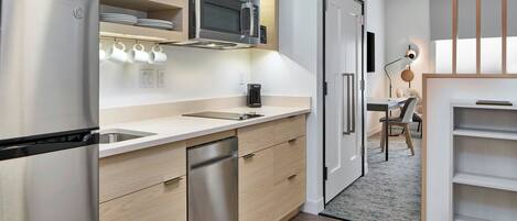 Eine moderne Küche mit Edelstahl-Kühlschrank, Mikrowelle und Geschirrspüler. Auf der Arbeitsfläche steht eine Kaffeemaschine, und im Hintergrund ist ein Essbereich zu sehen.