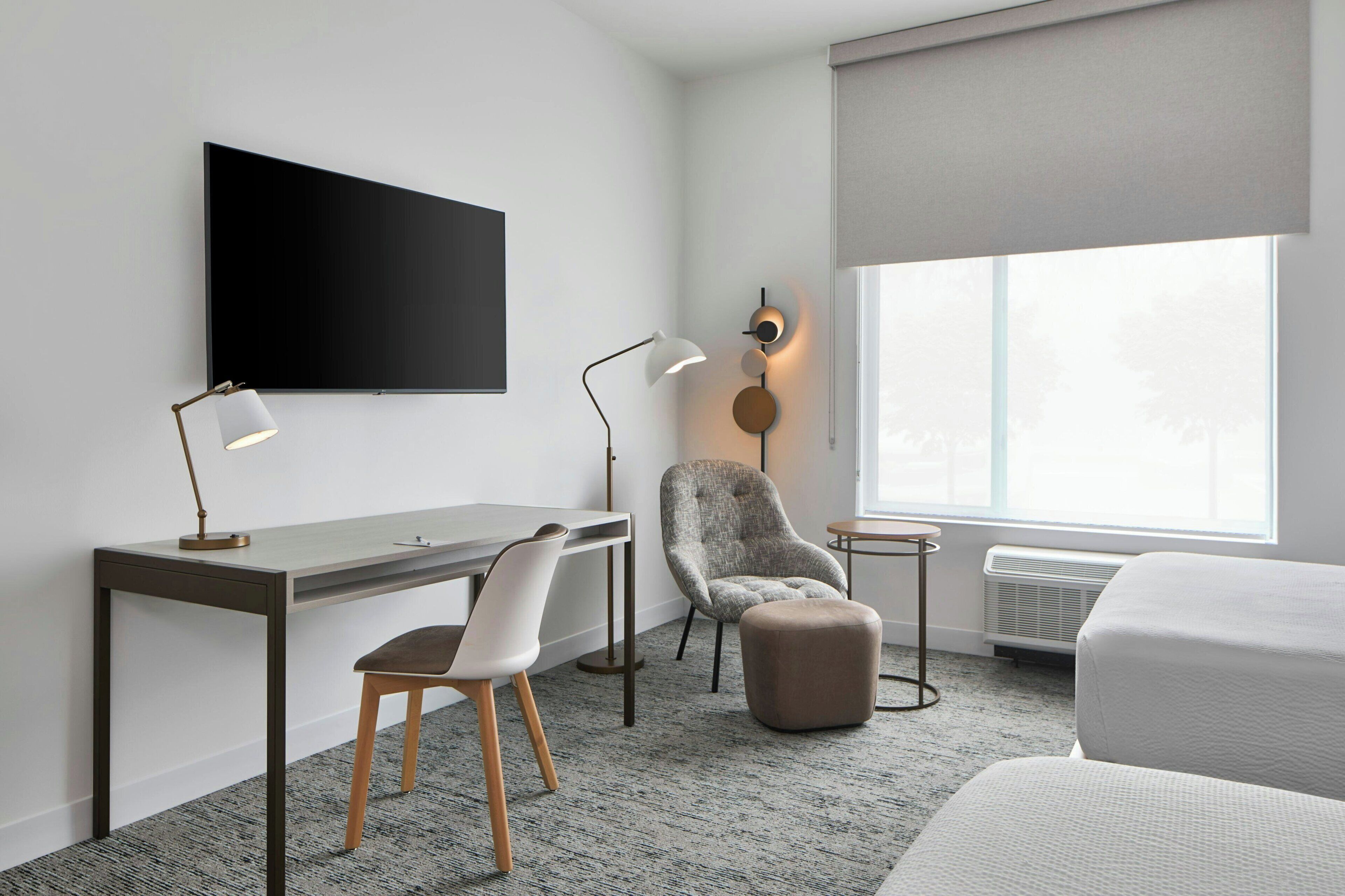 Habitación de hotel con escritorio, silla, reposapiés y un amplio ventanal.