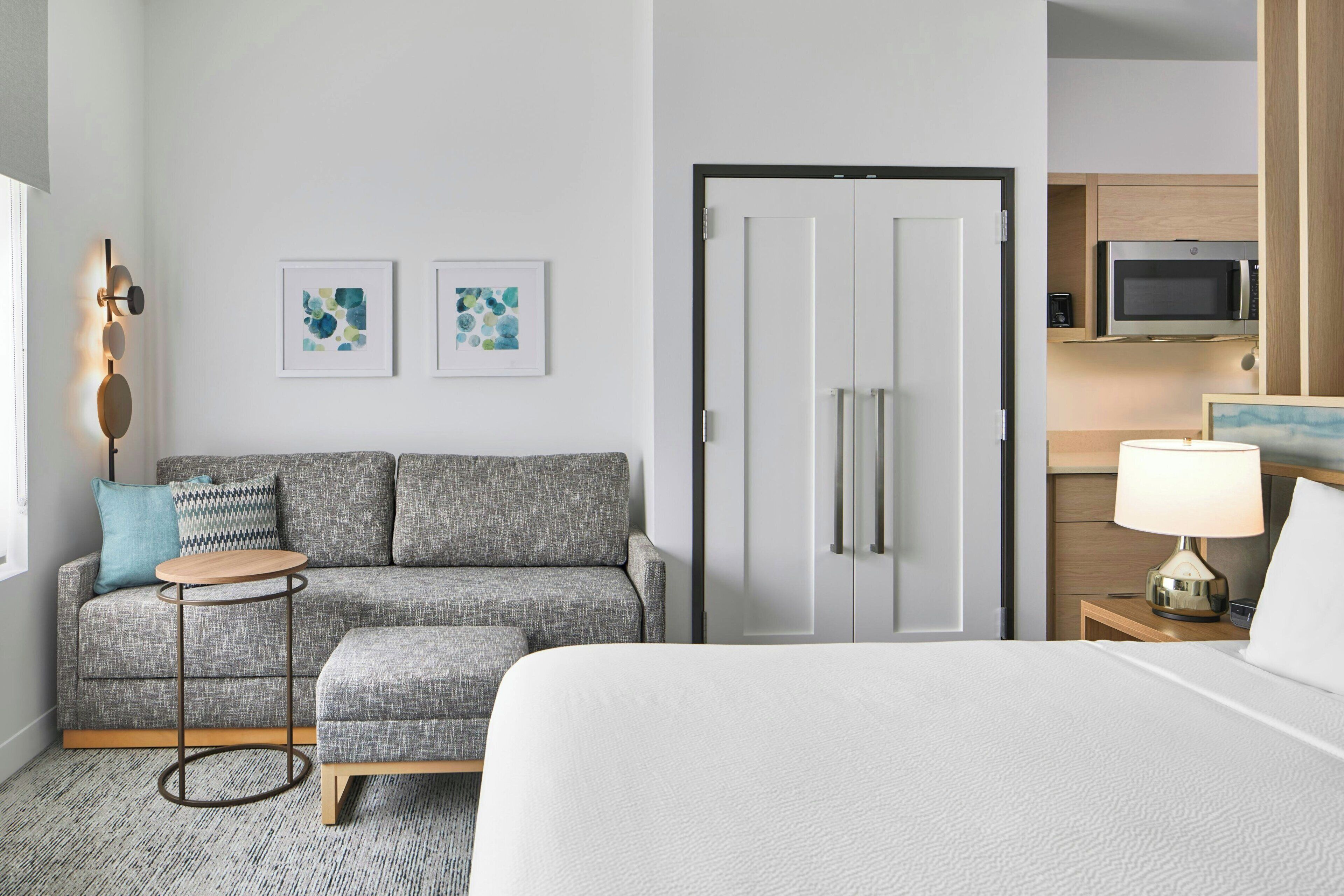 Habitación de hotel con cama, sofá, una mesita redonda, televisión y microondas en la zona de la cocina.