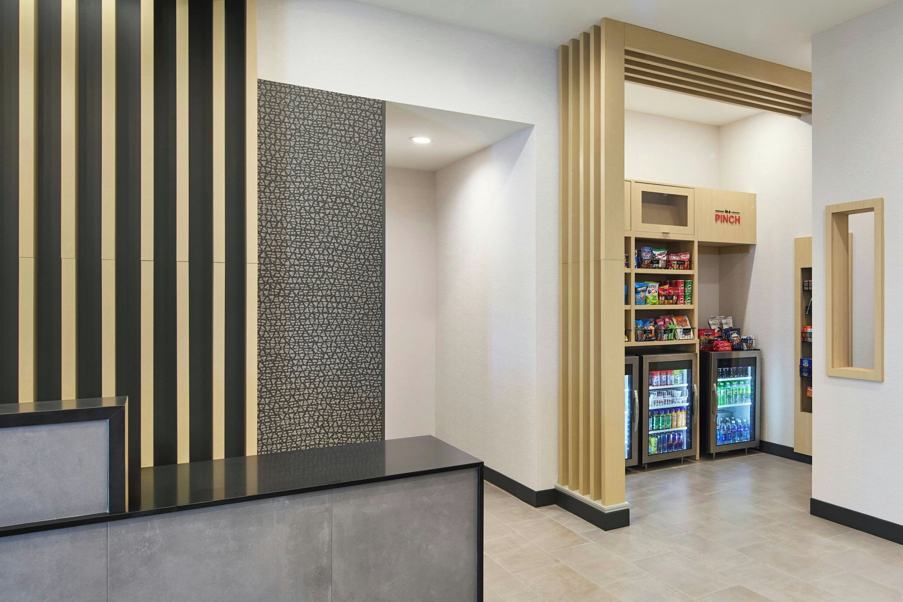 A reception area with a black reception desk, a patterned wall, vending machines, and a 'PINCH' sign.
