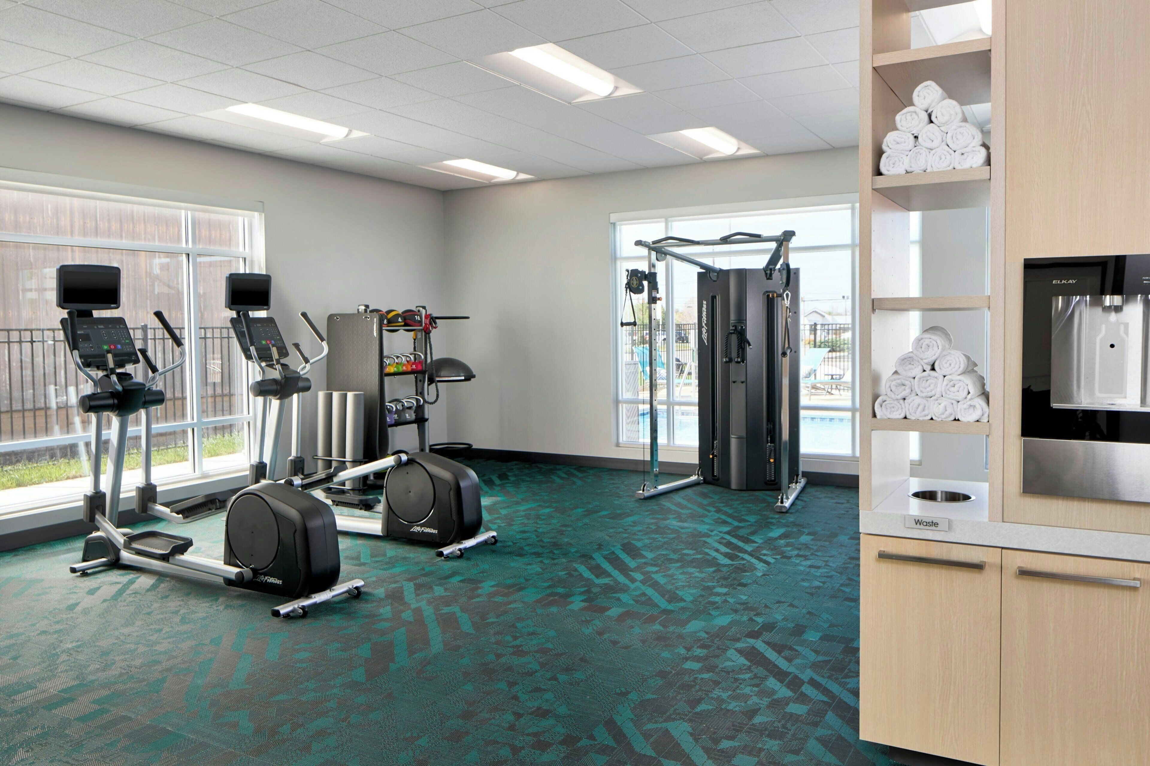 A gym with exercise equipment, large windows, and a water dispenser.