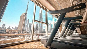 A gym with treadmills and a large window overlooking a cityscape with tall buildings. - DVH Luxe Retreat 4BR Burj View Apartment (Dubai)