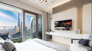 A modern hotel room with a large bed, a sofa, a TV mounted on the wall, and a balcony with a city view. - DVH Luxe Retreat 4BR Burj View Apartment (Dubai)