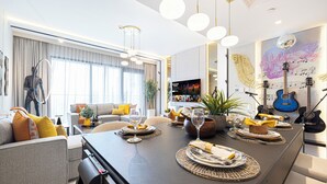 A modern dining area with a long table set for a meal, a sofa with cushions, a television, and a guitar wall art piece. - DVH Luxe Retreat 4BR Burj View Apartment (Dubai)