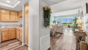 A spacious kitchen with wooden cabinets, a dining area with a sofa and table, and a view of a golf course through large windows. - Gorgeous Two Bedroom in Rancho Las Palmas (Rancho Mirage)