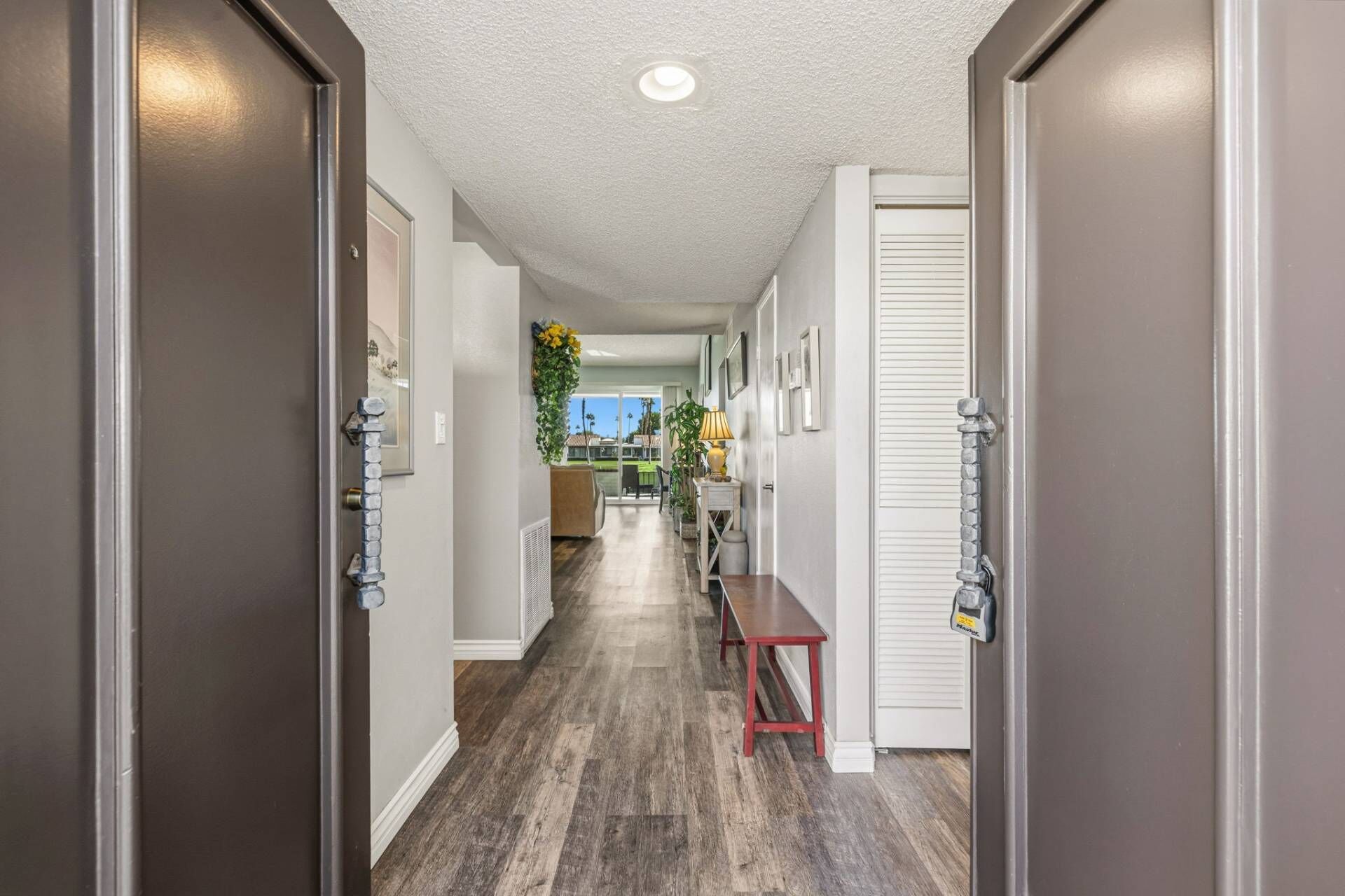 A hallway with wooden flooring, a bench, and a door with a security device.