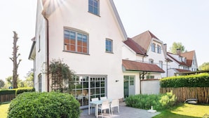 A two-story house with a large glass door and a patio with outdoor furniture.