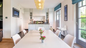 A modern kitchen with white cabinets, a central island, and a dining area with a long table and chairs.