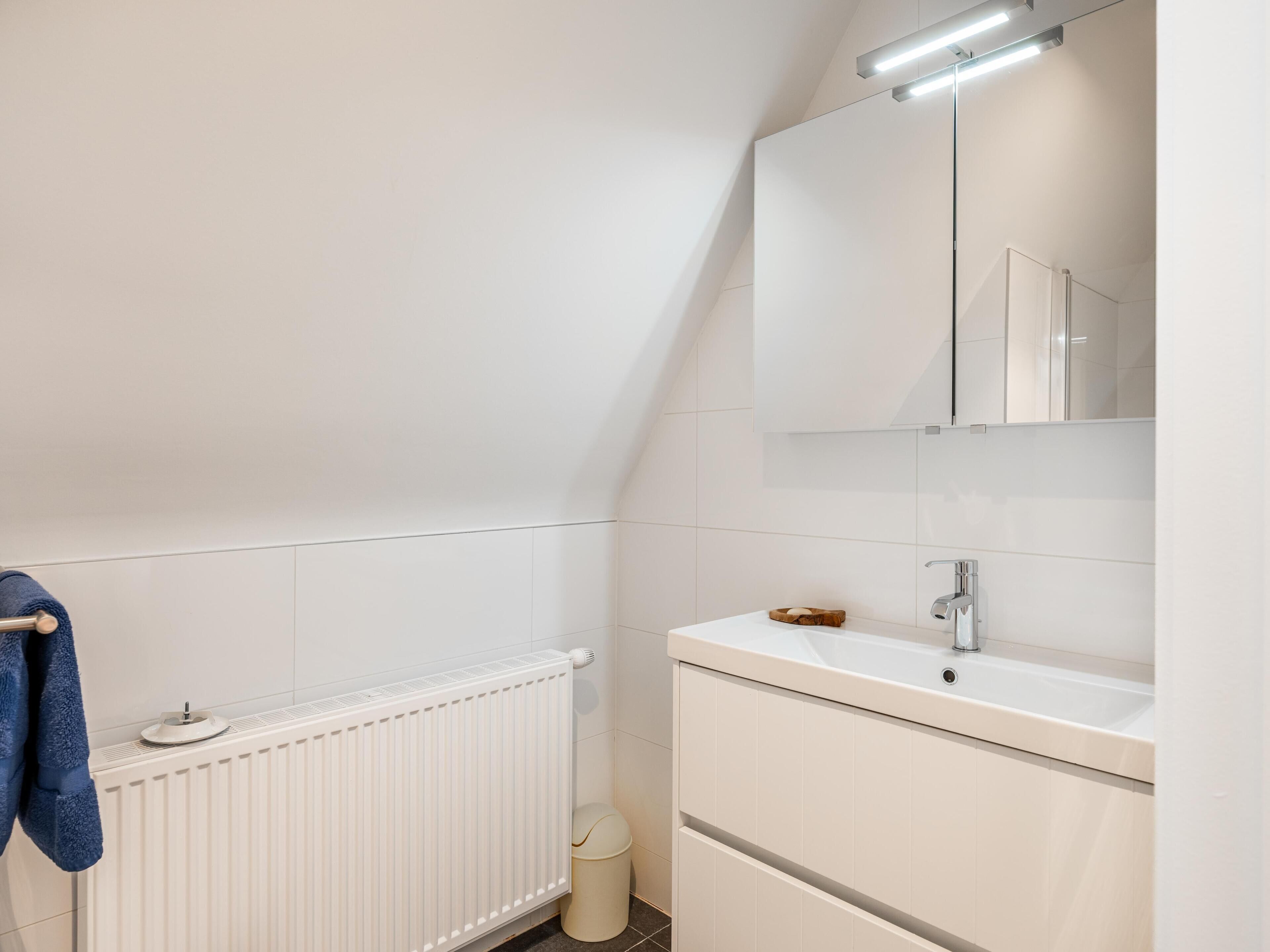 A modern bathroom with a white radiator, a sink with a mirror above it, and a towel hanging on a rack.