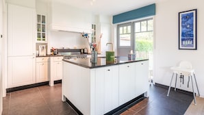 A modern kitchen with white cabinetry, a central island, and a window with a view of greenery.