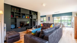 A modern living room with a large flat-screen TV, dark sofas, and a wooden coffee table.