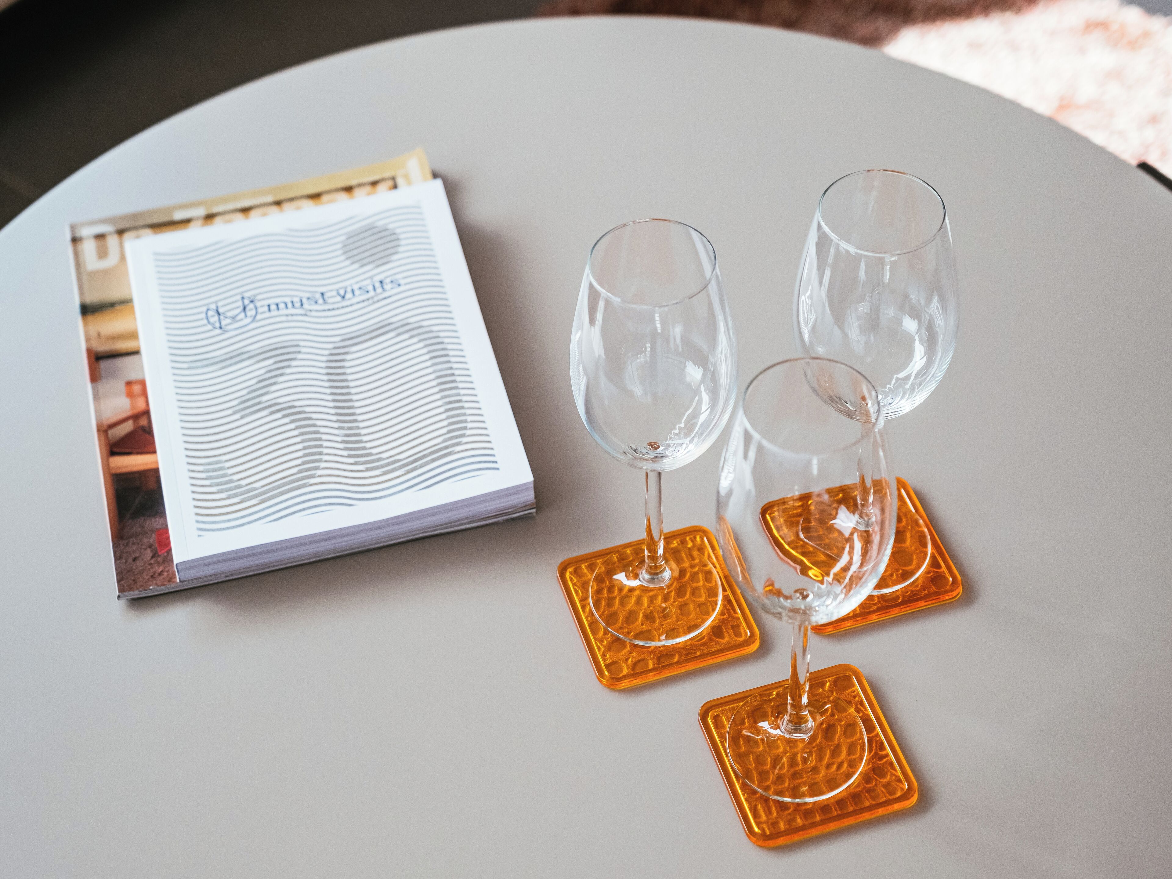 A table with a magazine, two wine glasses, and two square coasters.