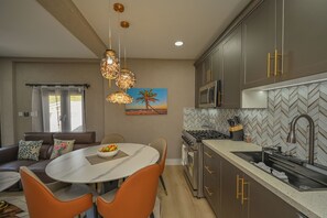 Et moderne køkken med et backsplash i fiskebensmønster, rustfrie stålens apparater og et spiseområde med et marmorbord og orange stole.