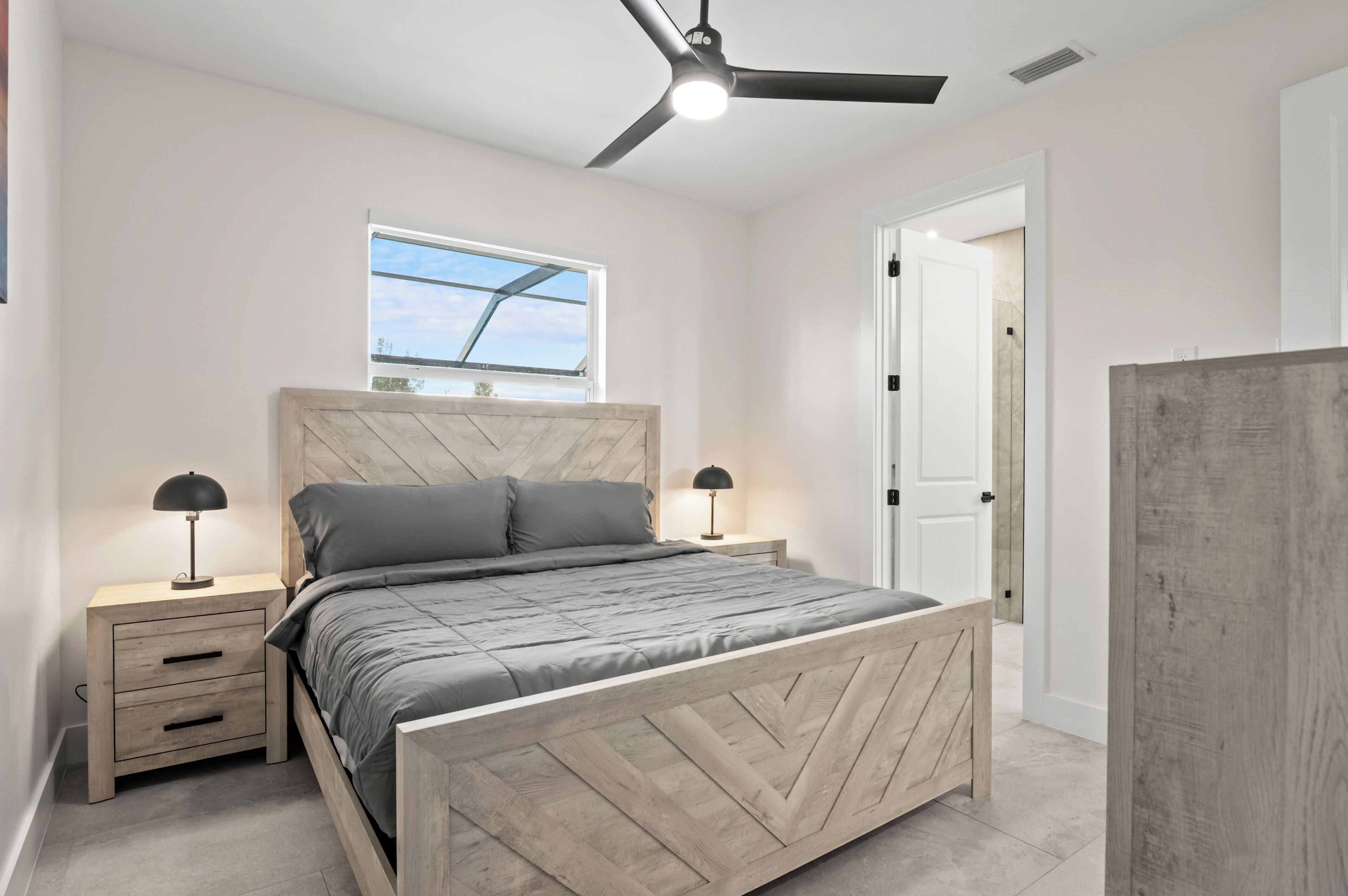 A bedroom with a bed, nightstands, a ceiling fan, a window, and a door.