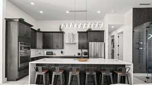 A modern kitchen with dark cabinets, stainless steel appliances, and a central island with bar stools. - Intervillas Florida - Villa Dolphin (Cape Coral)