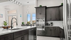 A modern kitchen with dark cabinets, stainless steel appliances, and a white countertop. - Intervillas Florida - Villa Dolphin (Cape Coral)