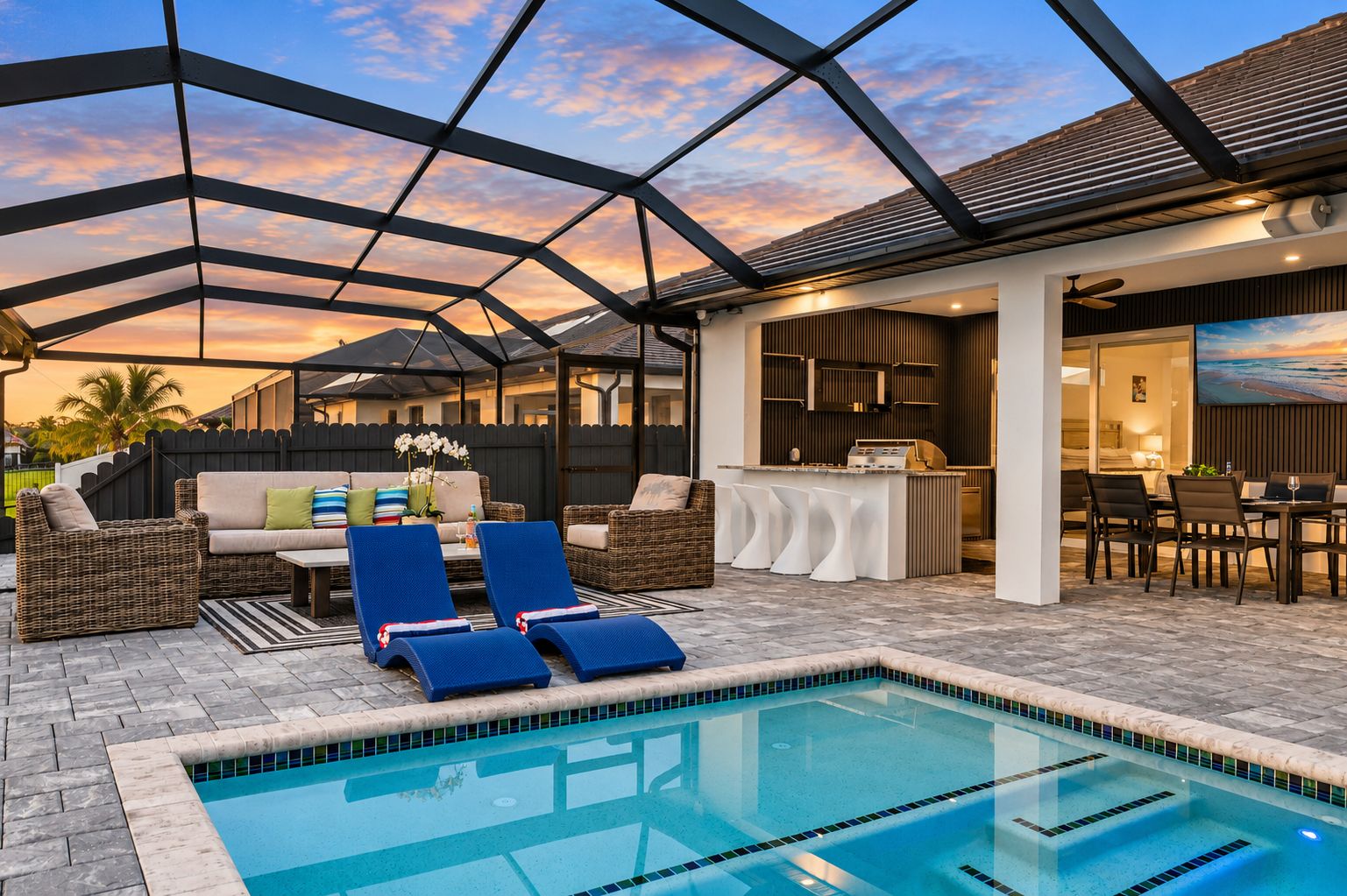 A pool area with lounge chairs, a dining area, and a kitchen.