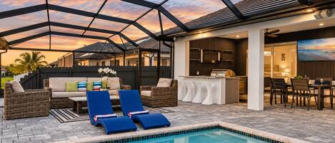 A pool area with lounge chairs, a dining area, and a kitchen.