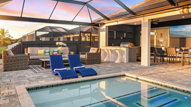 A pool area with lounge chairs, a bar, and a seating area with a view of the sunset. - Intervillas Florida - Villa Dolphin (Cape Coral)