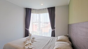 A hotel room with a neatly made bed, a large window with curtains, and a ceiling light.