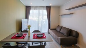 A modern dining area with a table set for two, a sofa, and a large window with curtains.